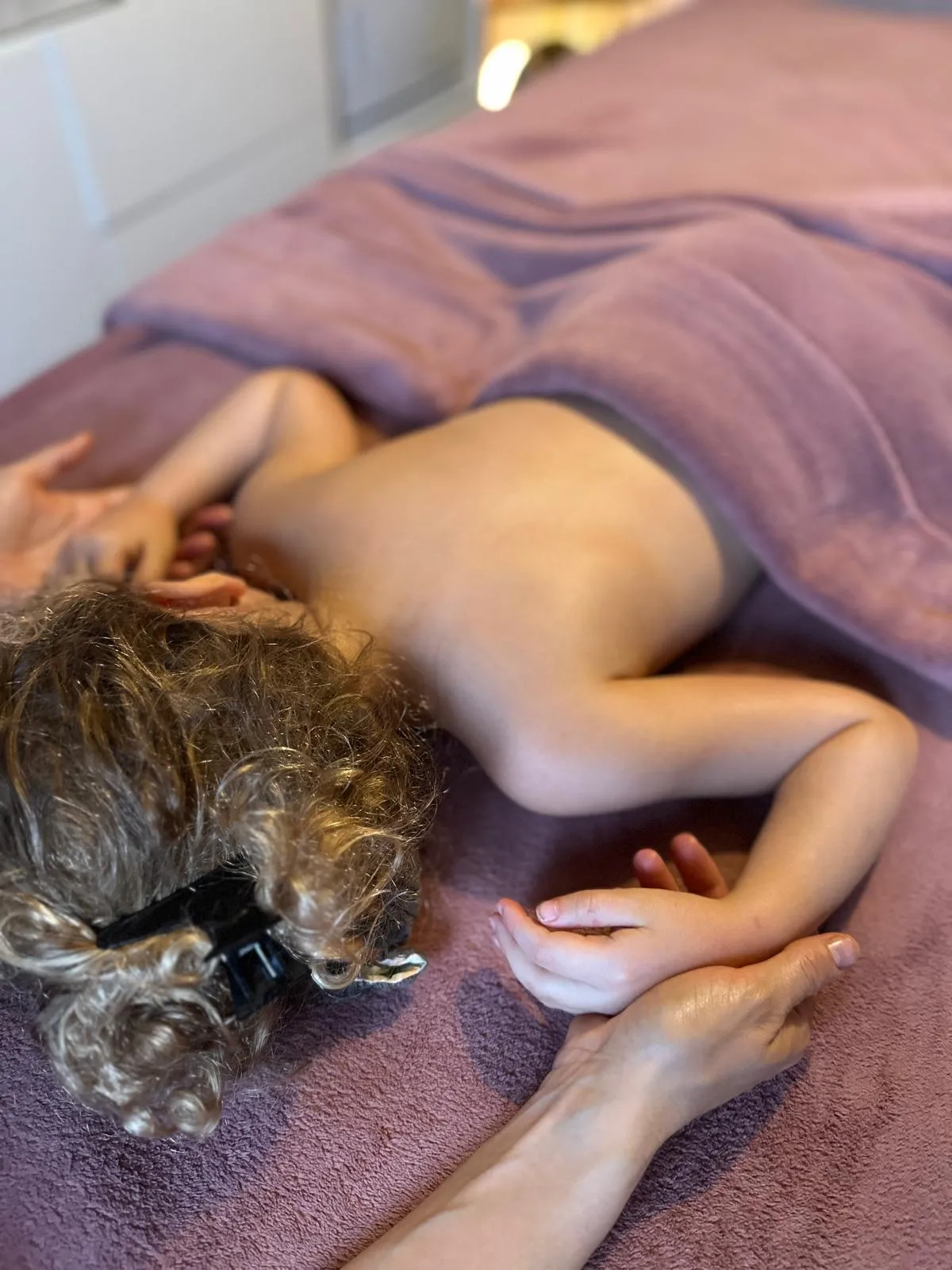 Massage du dos d'un enfant allongé sous un drap, dans la lumière douce de l'Institut